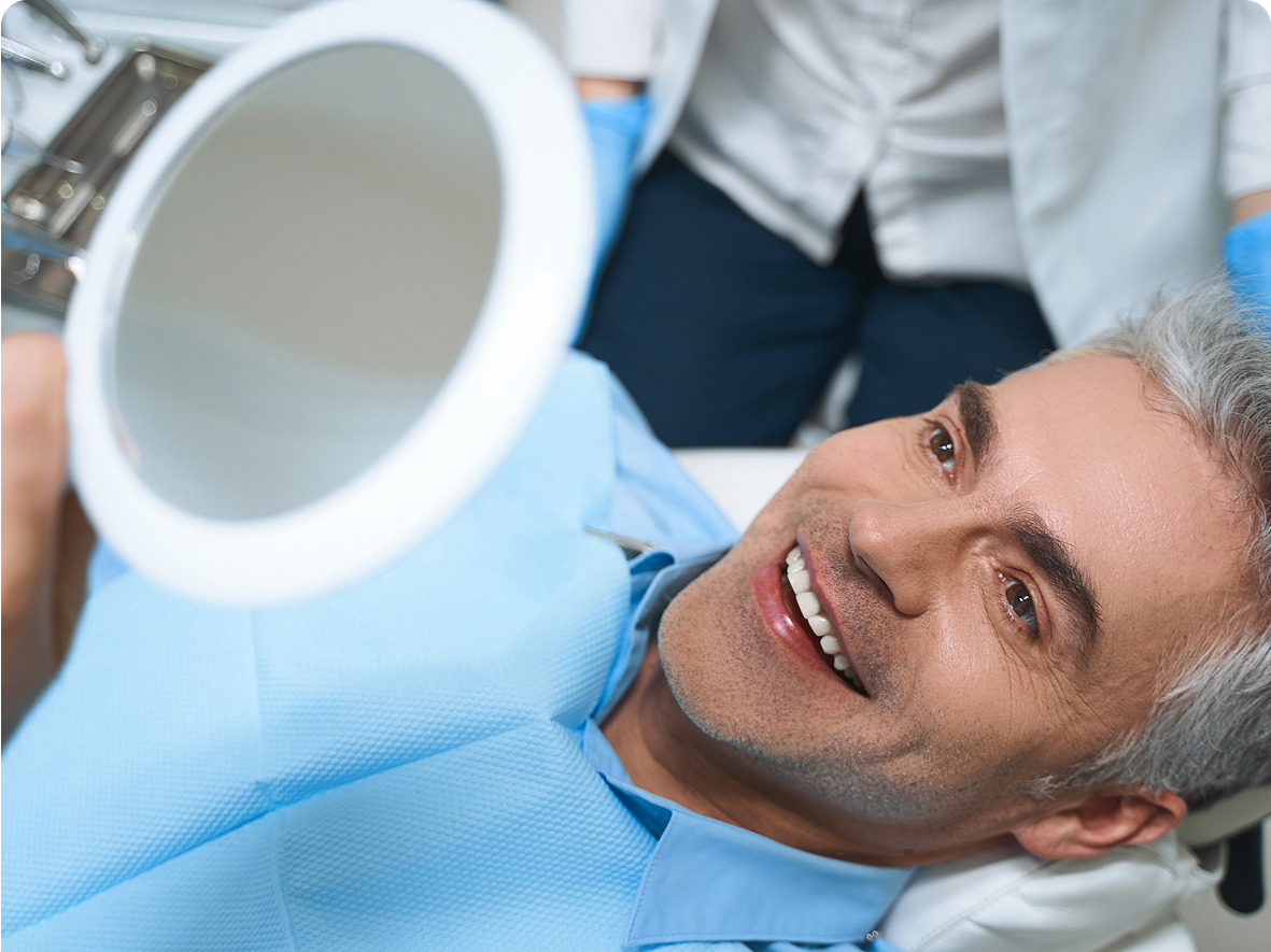 Man smiling, holding mirror in dental office.