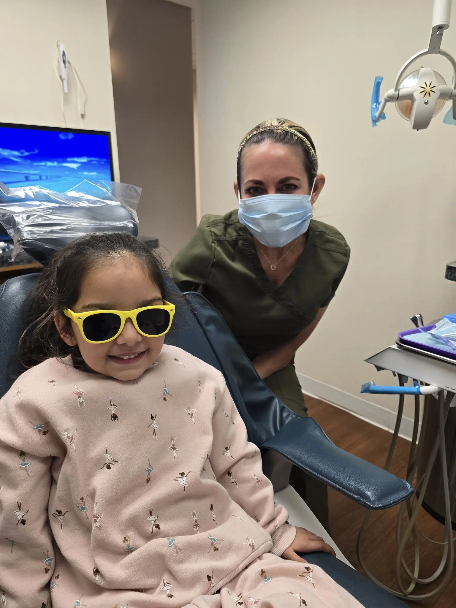 Young girl in sunglasses smiling with nurse in mask.