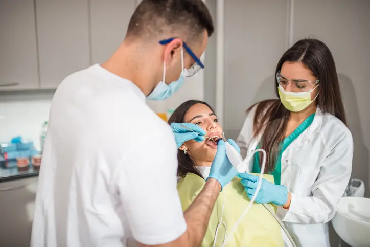 Dentist examining a patient's teeth with an assistant present.
