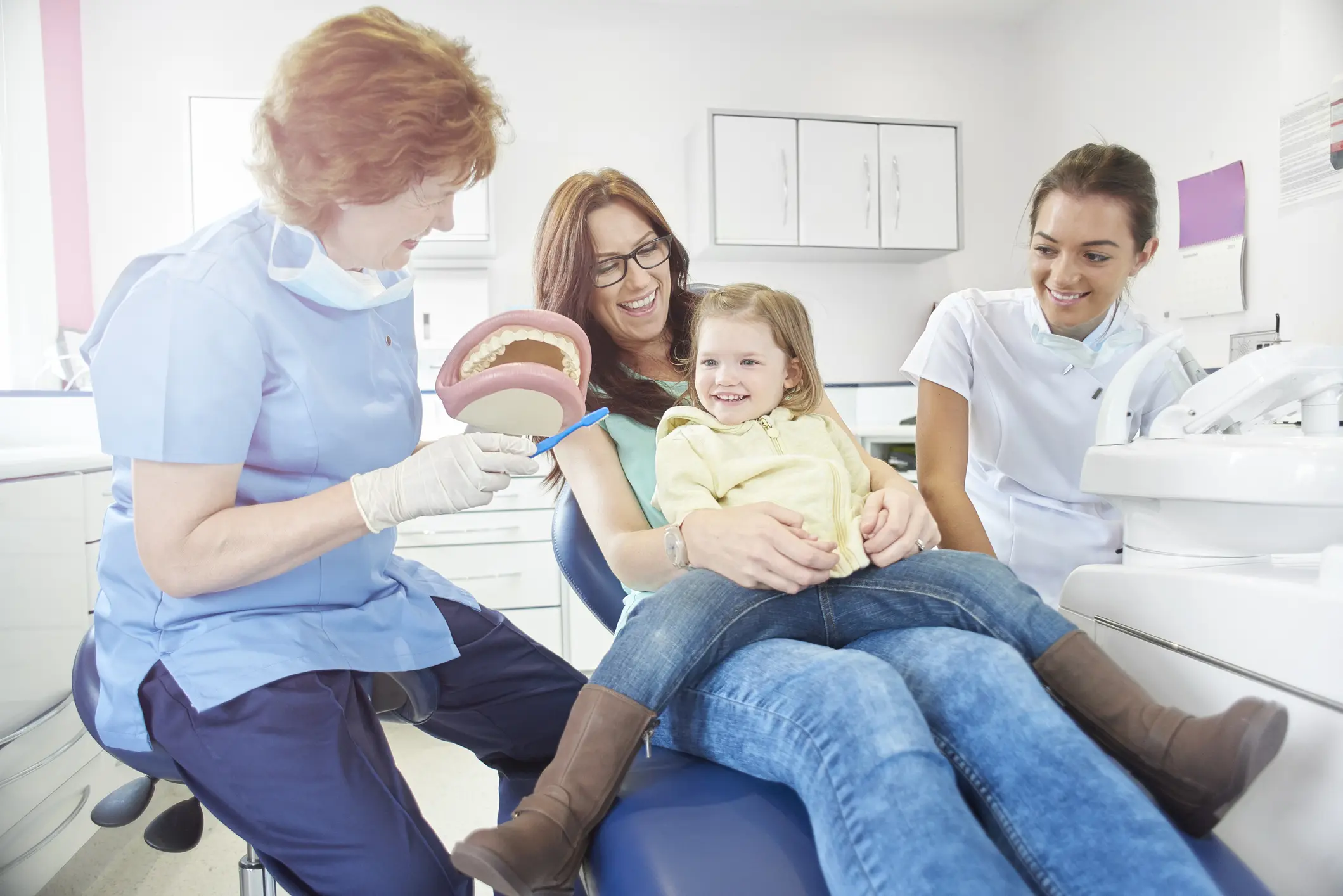 A young girl at the dentist with her mother and dental staff.