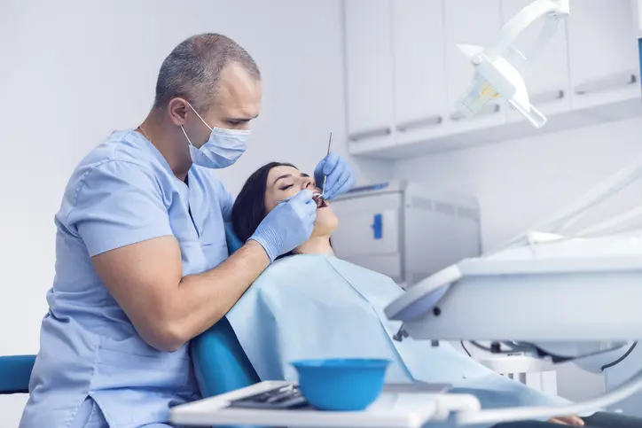 Dentist examining a patient's mouth wearing protective gear.