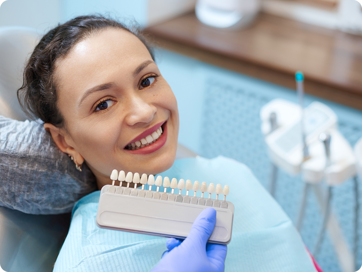 Woman smiling in dental clinic with shade guide.
