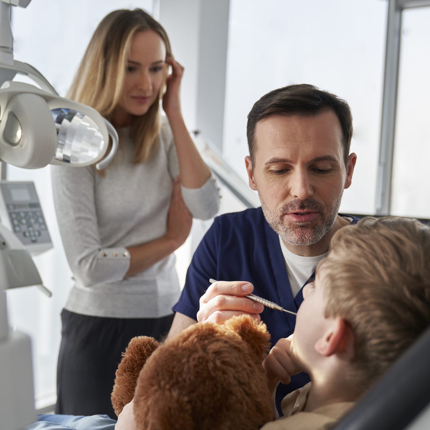 Dentist examining a patient while an assistant looks on.